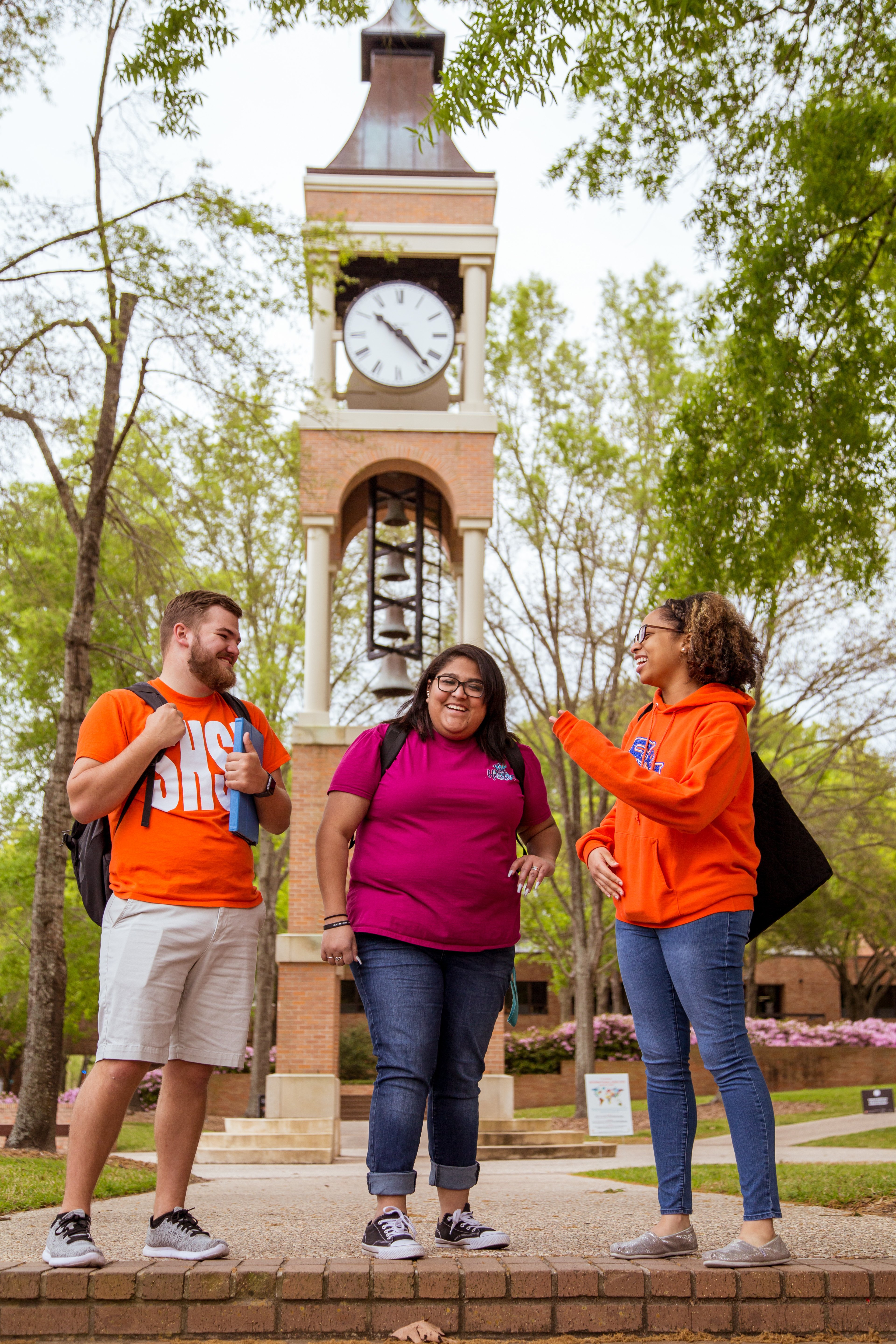 Three students smiling and talking in front of clock tower.
