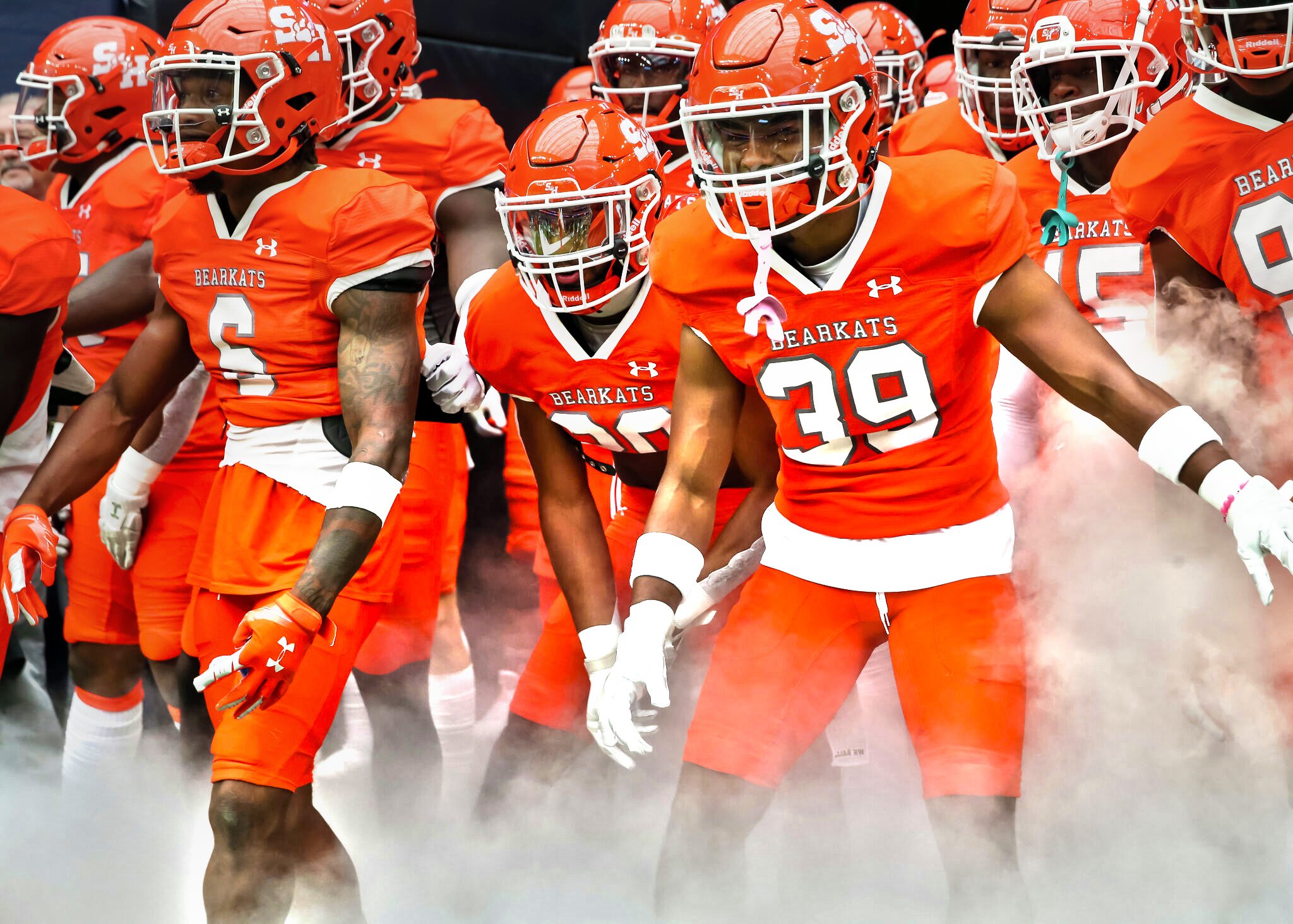 Football players dressed in orange uniforms walking through fog.