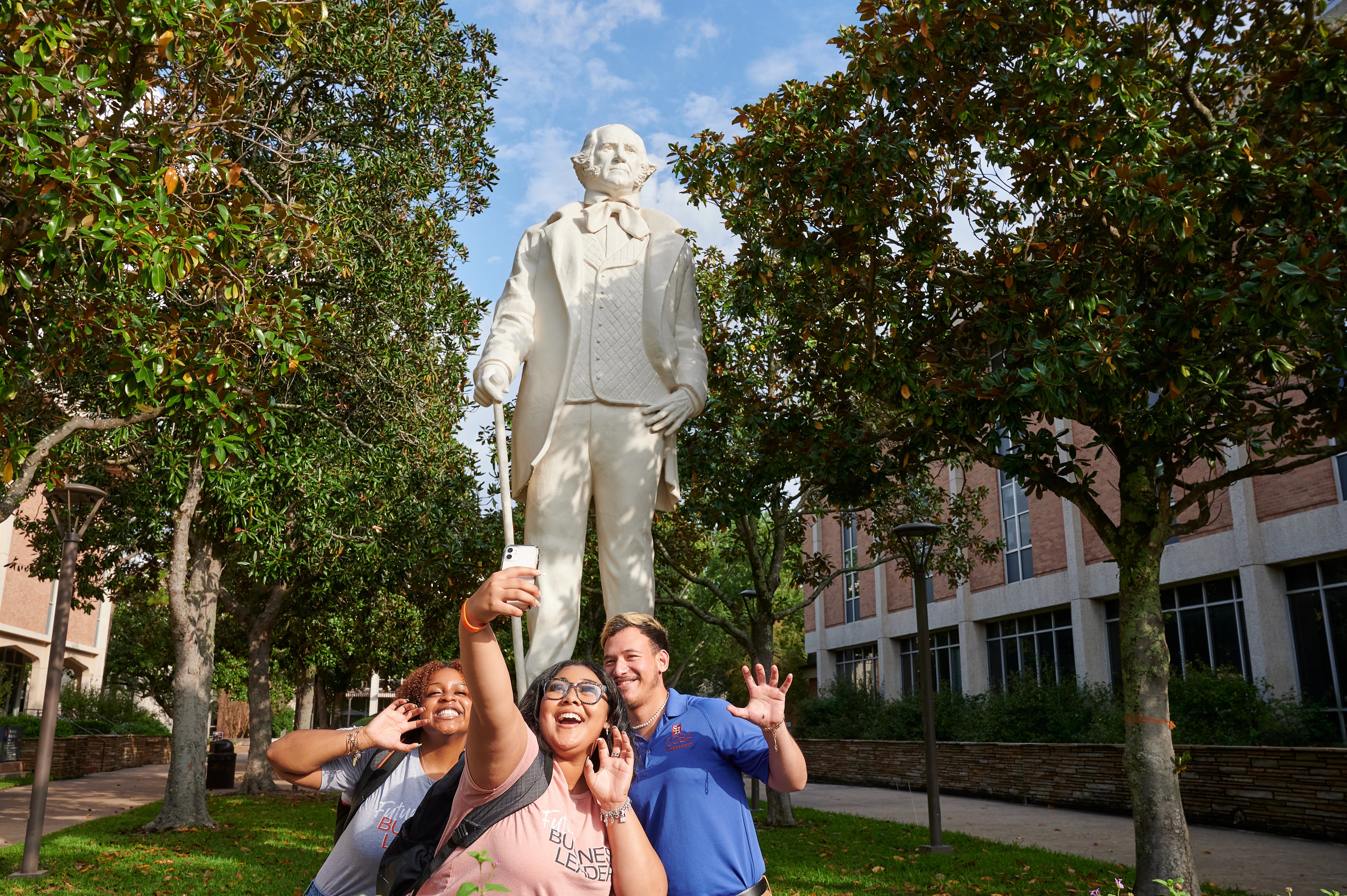 Three students taking a selfie in front of Sam Houston statue.