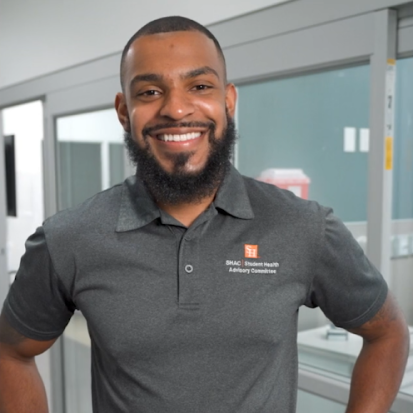 A young man wearing a grey polo shirt smiling at the camera.